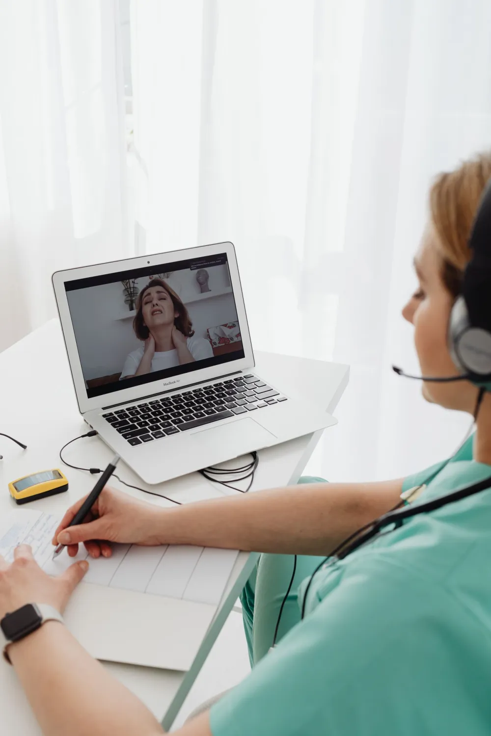 Veterinária de pijama cirúrgico verde e headset atende por videochamada no notebook